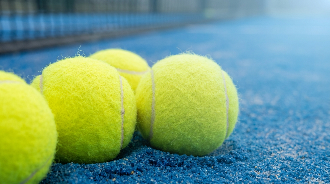 Gelbe Padelbälle auf dem blauen Sandplatz